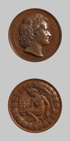 F5 Medaljens forside: Portræt af Thorvaldsen. Medaljens bagside: Billedhuggerkunstens genius knæler med Gratierne og Amor i hånden