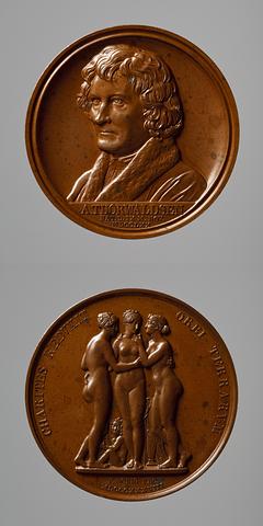 F12 Medaljens forside: Portræt af Thorvaldsen. Medaljens bagside: Gratierne og Amor